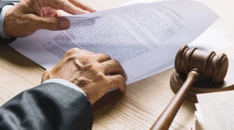 lawyer-s-hand-holding-document-with-gavel-mallet-wooden-desk